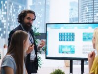 Financial advisor presents detailed stock market analysis to clients on big screen, helping them make informed investment decisions. Broker in office providing family with financial analysis, camera A